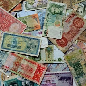 Può includere: Una collezione di banconote di carta colorate provenienti da diversi paesi, tra cui Stati Uniti, Italia, Portogallo e Cina. Le banconote sono disposte in uno schema casuale, con alcune sovrapposte. Le banconote sono in vari stati di usura, alcune sono più sbiadite di altre.