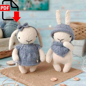 May include: Two knitted bunny amigurumi toys with blue and white accents. The bunny on the left is wearing a blue dress and a bow. The bunny on the right is wearing a blue hat and scarf.