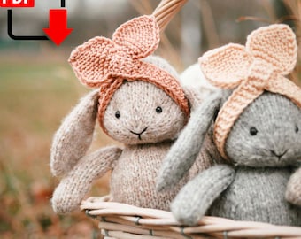 May include: Two knitted bunny toys with pink and gray yarn, wearing pink headbands, sitting in a wicker basket.