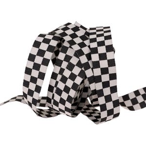 May include: A length of black and white checkered ribbon, tightly coiled. The ribbon's pattern is a classic checkerboard design, with alternating black and white squares. The ribbon is likely made of a woven fabric.
