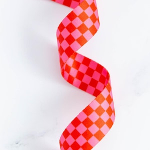 May include: A vibrant, checkered ribbon in shades of red and pink, spiraling against a white background. The ribbon's pattern features a repeating square design, creating a bold and eye-catching visual. Ideal for crafting and gift wrapping.