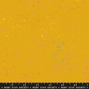 May include: Mustard yellow fabric with a speckled design. The fabric features a textured surface and is adorned with colorful paint splatters in shades of pink, yellow, and blue. The text "RUBY STAR SOCIETY" is printed at the bottom.
