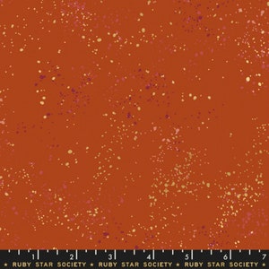 Puede incluir: Tela de color óxido con un diseño moteado. La tela presenta pequeños puntos irregulares en tonos amarillos, rosas y morados. El texto "RUBY STAR SOCIETY" está impreso en la parte inferior.