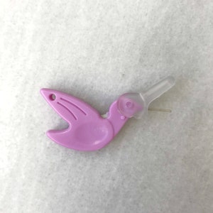 May include: A purple plastic threader shaped like a bird with a clear plastic needle.
