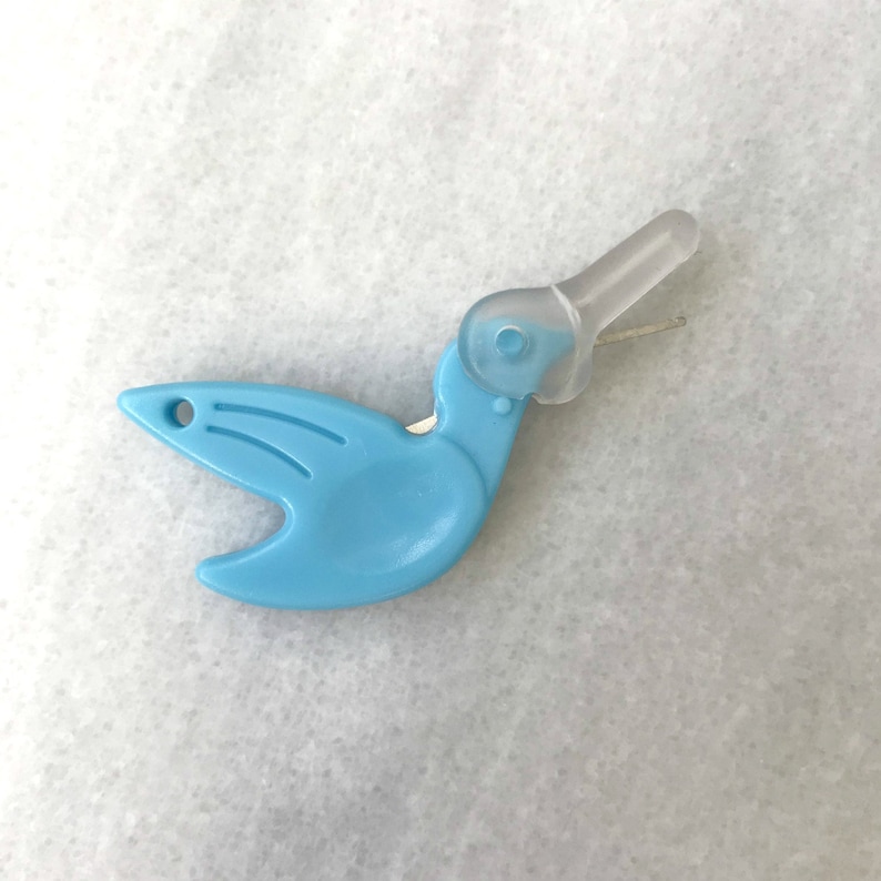 May include: A light blue plastic bird-shaped thread cutter with a clear plastic handle. The cutter has a small hole on the side of the bird's body.
