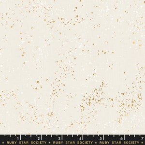 Peut inclure: Tissu crème avec un motif tacheté de points dorés et blancs. Le tissu a une texture subtile et convient à divers projets de couture. Le texte "RUBY STAR SOCIETY" est imprimé en bas.