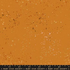 May include: Close-up of a fabric with a textured, orange-brown background. The fabric is speckled with various sized dots in shades of white, brown, and gold. The text "RUBY STAR SOCIETY" is printed at the bottom.