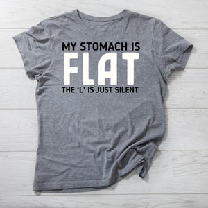May include: A gray t-shirt with the text "My stomach is FLAT. The 'L' is just silent." printed in white.