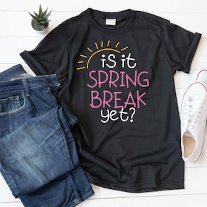 May include: Black t-shirt with a yellow sun and pink text that reads "is it spring break yet?"