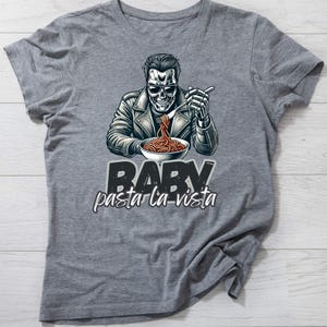 May include: A gray t-shirt with a graphic of a skeleton wearing a leather jacket and sunglasses, eating spaghetti. The text "BABY pasta la vista" is printed below the graphic.