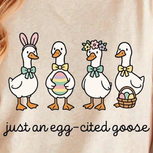 May include: A cream-colored t-shirt featuring a whimsical illustration of four cartoon geese. Each goose is adorned with Easter-themed accessories, including bunny ears, a decorated egg, and floral crowns. The text "just an egg-cited goose" is written in a playful script.