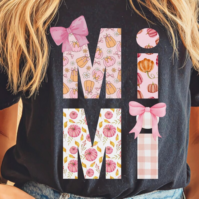May include: Black t-shirt with the word "MIMI" in a fall-themed design. The letters are filled with pumpkins and floral patterns in pink and orange. Pink bows accent the letters, creating a festive autumn look.