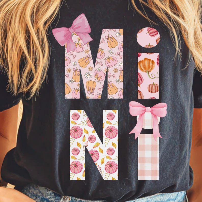 May include: Black t-shirt with the word "MINI" in a fall-themed design. The letters are filled with pumpkin and floral patterns, and accented with pink bows. The "I" is a vertical rectangle with pumpkins.