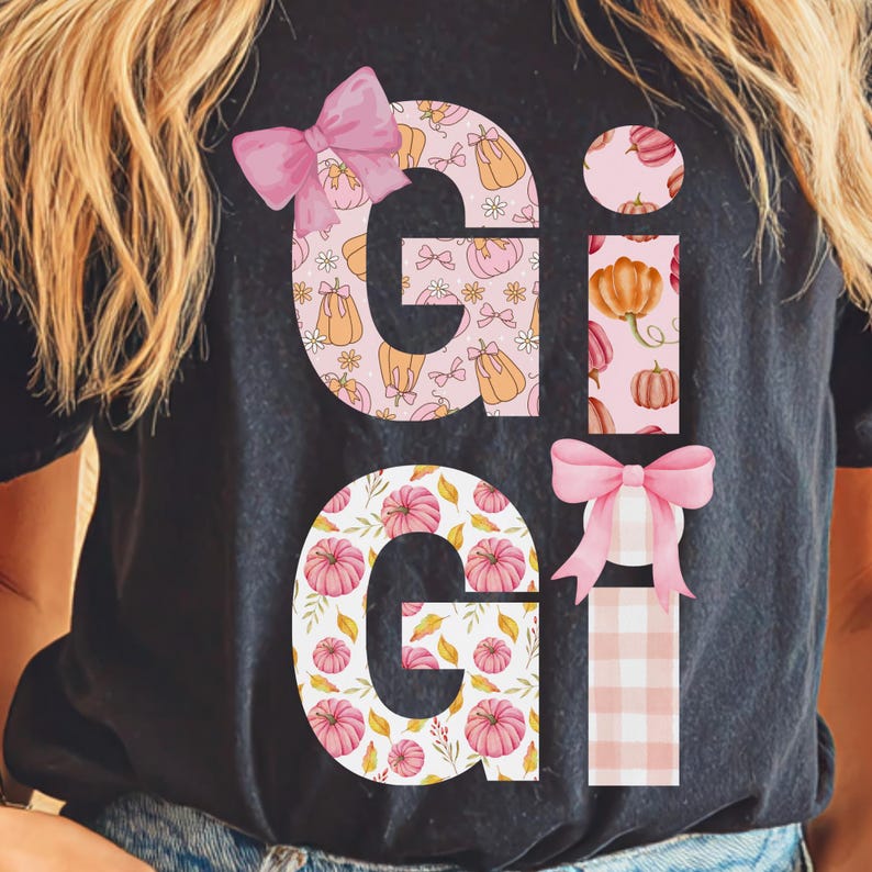 May include: Black t-shirt with the name "GiGi" in a fall-themed design. The letters are decorated with pumpkins, bows, and floral patterns in shades of pink, orange, and white.