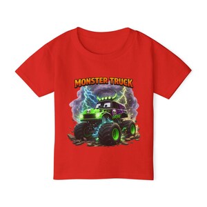 May include: A red short-sleeved t-shirt featuring a graphic of a green and black monster truck with a skull design. The text "MONSTER TRUCK" is displayed above the truck, with lightning bolts in the background.
