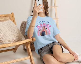 Könnte beinhalten: Ein hellblaues Kurzarm-T-Shirt mit einem Grafikdruck aus Regenbogen, Musiknoten und dem Text "can you say MAMA?", der ein Foto einer Person in rosa Hemd und Jeanslatzhose umrahmt, kombiniert mit grauen Jeansshorts.