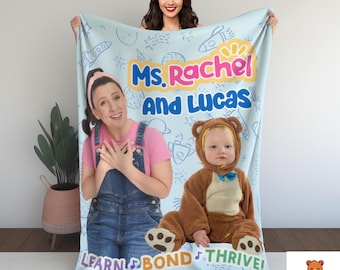 May include: A light blue blanket featuring the text "Ms. Rachel and Lucas" with images of Ms. Rachel and a baby in a bear costume. The blanket has a light blue background with doodles and the words "Learn, Bond, Thrive!"