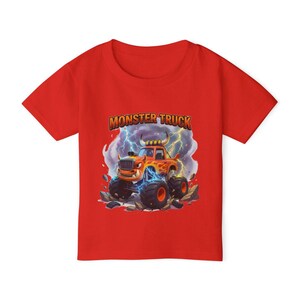 Puede incluir: Camiseta roja de manga corta con un dise&ntilde;o de cami&oacute;n monstruo de dibujos animados. El gr&aacute;fico incluye el texto "MONSTER TRUCK" encima del cami&oacute;n, que es naranja y amarillo con rayos azules.