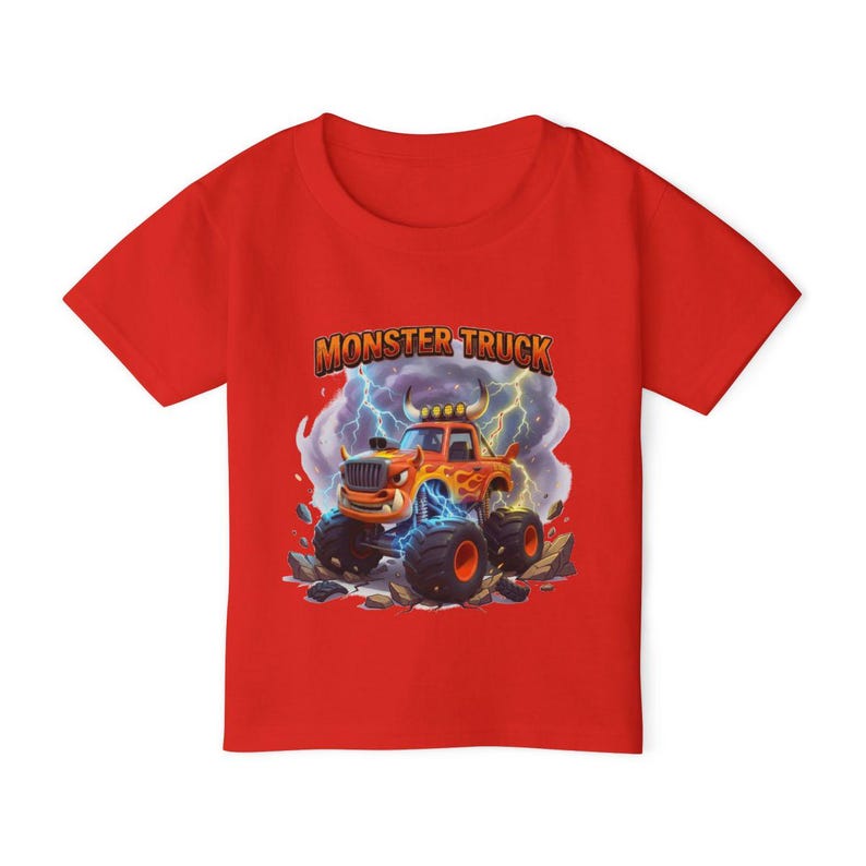 Puede incluir: Camiseta roja de manga corta con un dise&ntilde;o de cami&oacute;n monstruo de dibujos animados. El gr&aacute;fico incluye el texto "MONSTER TRUCK" encima del cami&oacute;n, que es naranja y amarillo con rayos azules.