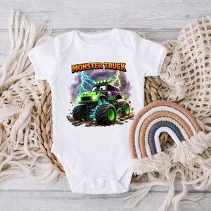 May include: White baby bodysuit with a colorful graphic of a green monster truck with black tires, a skull, and the text "MONSTER TRUCK". The design includes lightning bolts and a purple and black background.
