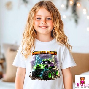 May include: White t-shirt featuring a colorful monster truck graphic. The design includes a green and purple monster truck with lightning bolts and the words "MONSTER TRUCK" in orange and yellow.