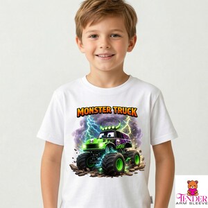 May include: White t-shirt featuring a colorful monster truck graphic with the text "MONSTER TRUCK". The monster truck is green and black with lightning bolts in the background. The shirt is worn by a young boy.
