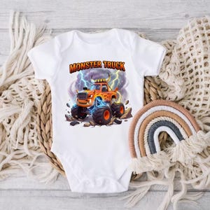 Puede incluir: Body de beb&eacute; blanco con un gr&aacute;fico colorido de un cami&oacute;n monstruo naranja con llamas, rayos y el texto "MONSTER TRUCK". El dise&ntilde;o est&aacute; sobre un fondo de cielo tormentoso.