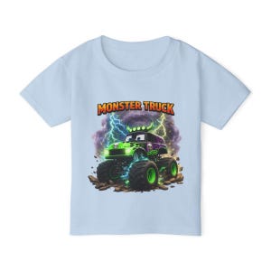 May include: Light blue t-shirt featuring a colorful graphic of a monster truck with green and purple accents, lightning bolts, and the text "MONSTER TRUCK". The design includes a skull and flames.
