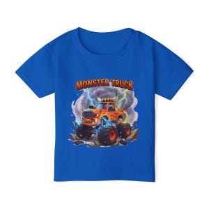 Puede incluir: Una camiseta azul con un gr&aacute;fico de un cami&oacute;n monstruo naranja con llamas, neum&aacute;ticos grandes y el texto "MONSTER TRUCK". El dise&ntilde;o incluye rayos y un suelo rocoso.