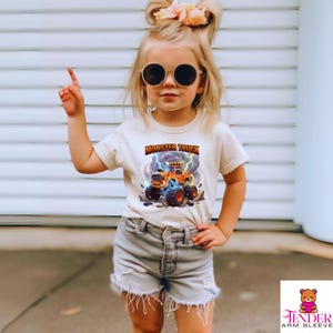 Puede incluir: Una camiseta color crema con un gr&aacute;fico de monster truck colorido y el texto "MONSTER TRUCK". El gr&aacute;fico incluye rayos y una ilustraci&oacute;n detallada del cami&oacute;n. La camiseta se combina con pantalones cortos de mezclilla.
