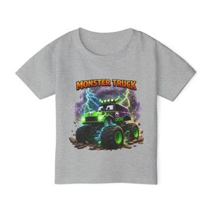 May include: A gray t-shirt featuring a colorful graphic of a monster truck. The monster truck is green and purple with large wheels, and the text "MONSTER TRUCK" is above it. Lightning bolts and rocks are in the background.