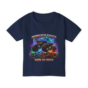 May include: Navy blue t-shirt featuring a colorful graphic of a monster truck with a shark-like design, the text "MONSTER TRUCK" and "BORN TO CRUSH". The design includes lightning bolts and a background of crushed cars.