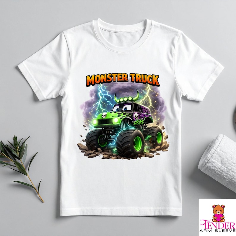 May include: White t-shirt featuring a colorful monster truck graphic. The monster truck is green and purple with large black tires and a skull design. The text "MONSTER TRUCK" is displayed above the truck in orange and yellow.