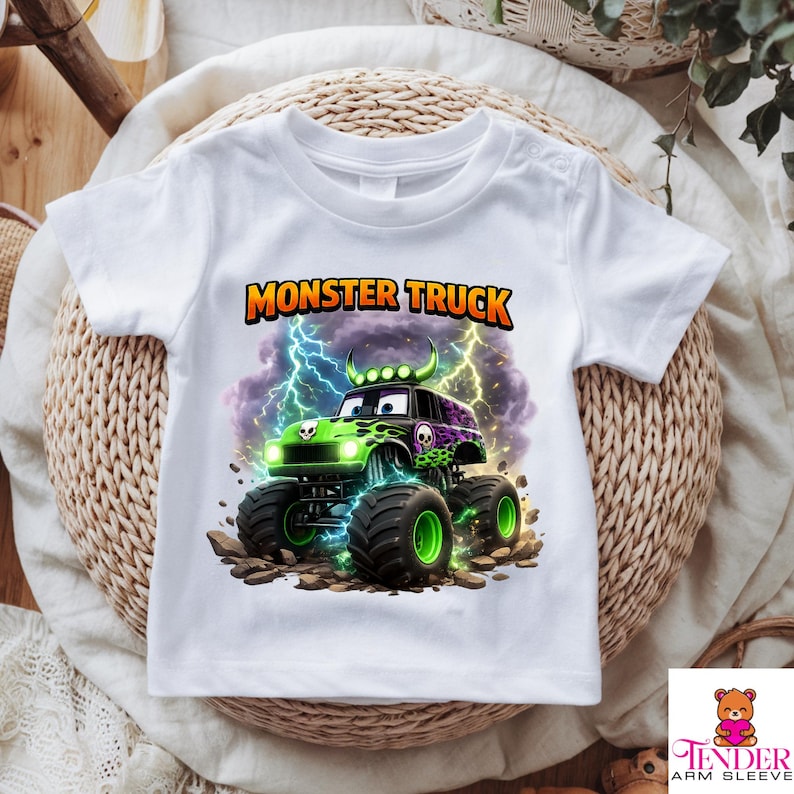 May include: White t-shirt featuring a colorful monster truck graphic. The design includes a green and black truck with skull details, large tires, and the text "MONSTER TRUCK" in orange and yellow. Lightning bolts are in the background.