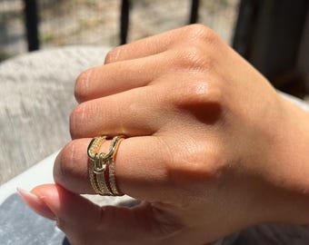 May include: A gold ring with three bands, each set with small clear stones. The ring is worn on a finger.