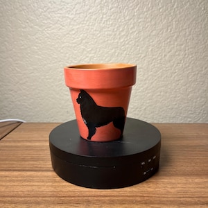 May include: A small terracotta flower pot painted a light pink color with a black silhouette of a dog on the side.