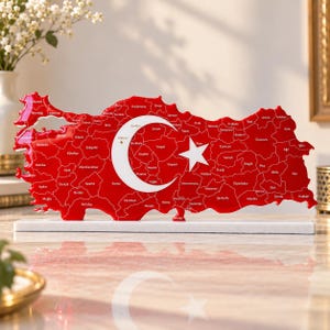 May include: A red map of Turkey shaped as a decorative object, featuring white outlines of provinces, city names, and a large white crescent and star symbol. The map is mounted on a rectangular white base, creating a freestanding display piece.
