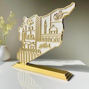 May include: A gold and white wooden decorative piece in the shape of a country's map, featuring detailed cutouts of landmarks and floral designs. The piece stands on a gold base, showcasing a layered design. The overall theme is a cultural or travel-related item.