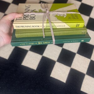 May include: A stack of four books tied together with twine. The top book is titled "THE PRUNING BOOK" with a green and white cover. The second book is also titled "THE PRUNING BOOK". The third book is green, and the bottom book is titled "THE FLAVORS OF BON APPÉTIT 19".