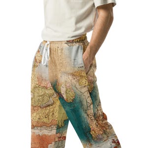 May include: Jogger pants with a vintage world map design in shades of beige, brown, and teal. The pants have a drawstring waist and pockets. The word "THE" is visible on the pocket.