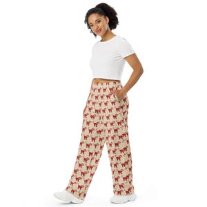 May include: Tan pants with a repeating pattern of red monkey illustrations. The pants have a wide leg design and pockets. The model is wearing a white crop top.