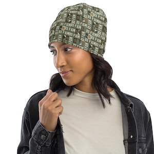 May include: A beanie hat with a repeating pattern of dollar bills in shades of green, brown, and white. The hat is worn by a person wearing a white shirt and a black denim jacket. The beanie is a stylish accessory.