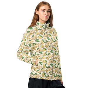May include: A cream-colored zippered jacket with a repeating pattern of ginger root and slices. The ginger is illustrated in a cartoon style with brown, yellow, and green colors.