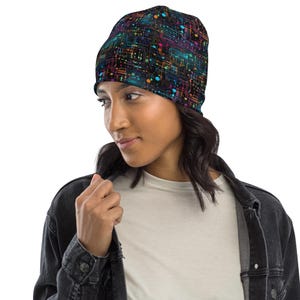 May include: A black beanie with a colorful circuit board design. The beanie features a pattern of neon blue, green, orange, and pink lines and dots. The hat is worn by a person wearing a white shirt and a black denim jacket.