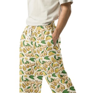 May include: Cream-colored drawstring pants with a repeating pattern of cartoon ginger root, slices, and green leaves. The pants have a relaxed fit and pockets. The ginger design is in shades of yellow and brown.