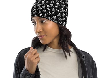 May include: Black beanie featuring a repeating pattern of white skulls and crossbones. The skull cap is worn by a person wearing a black denim jacket and a white t-shirt.