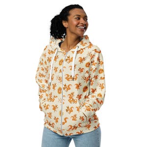 May include: A cream-colored zip-up hoodie with a repeating pattern of orange squirrels. The hoodie has a white zipper and a hood.