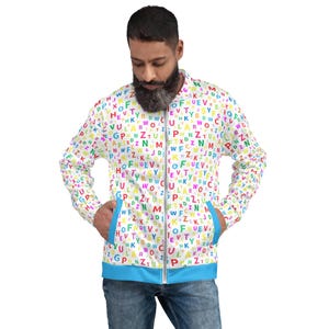 May include: A white bomber jacket with a colorful alphabet pattern. The jacket has a blue zipper and blue trim around the pockets.