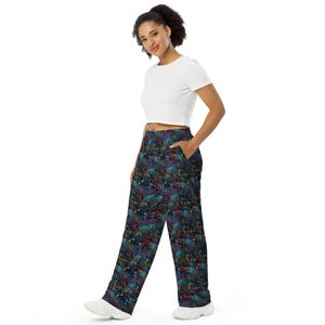 May include: Wide-leg pants with a colorful, abstract pattern in shades of blue, purple, and yellow. The pants have a dark background and a relaxed fit. The model is wearing a white crop top and white sneakers.