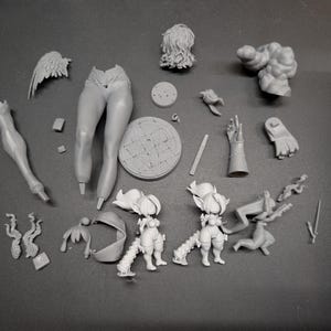 May include: A collection of unpainted, gray plastic model kit parts, including a pair of legs, a torso, a head, wings, and various other components. The parts are arranged on a gray surface, suggesting a miniature figure or character.